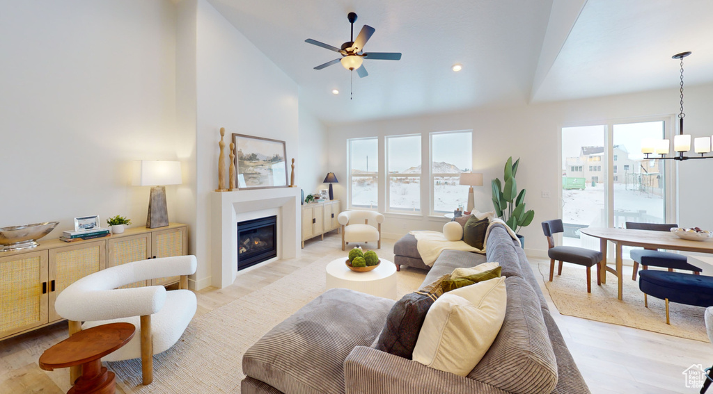 Living room with light wood-style floors, a glass covered fireplace, a chandelier, ceiling fan, and recessed lighting