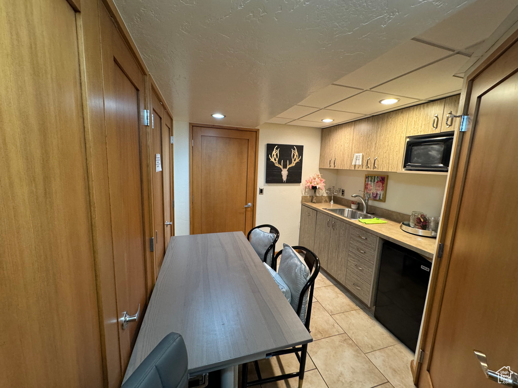 Kitchen with black appliances, light tile patterned floors, sink, and a textured ceiling