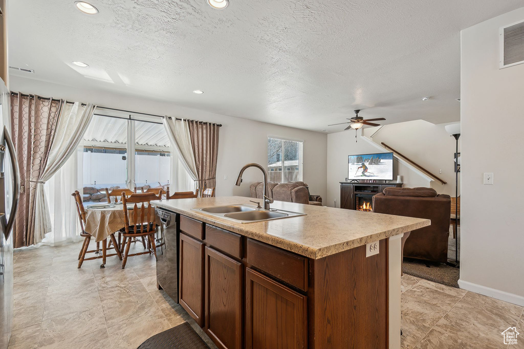 Kitchen featuring ceiling fan, sink, black dishwasher, a kitchen island with sink, and a textured ceiling