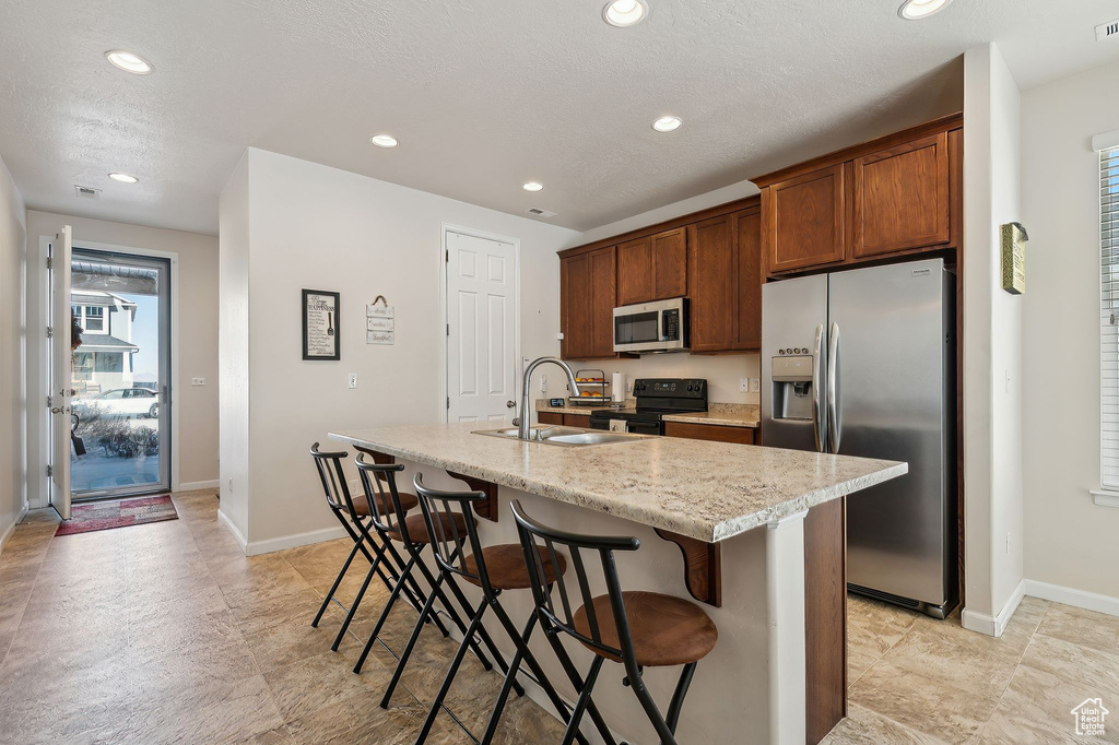 Kitchen with a kitchen bar, appliances with stainless steel finishes, a kitchen island with sink, light stone counters, and sink