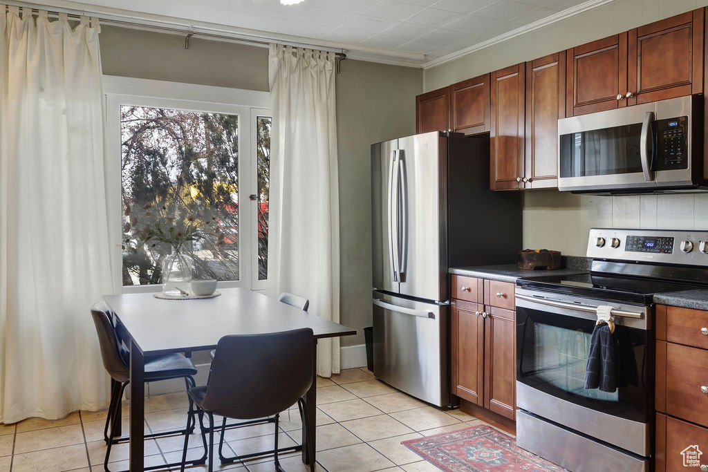 Kitchen featuring light tile patterned flooring, stainless steel appliances, and ornamental molding