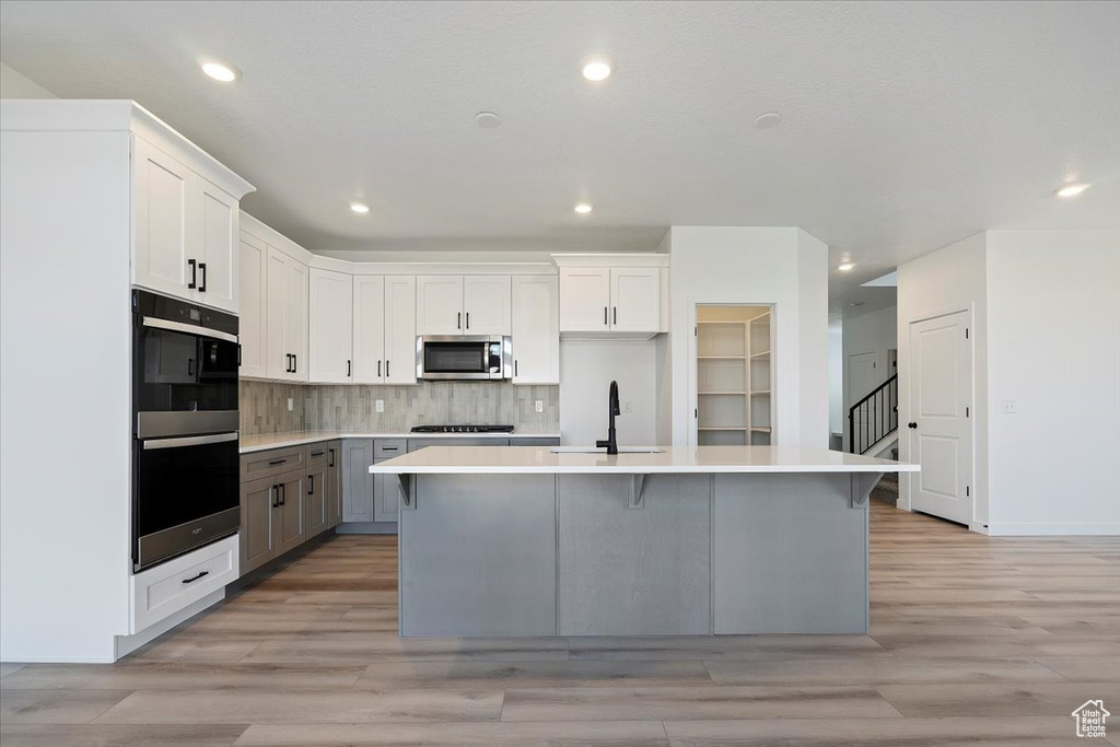 Kitchen featuring white cabinetry, stainless steel appliances, sink, and a center island with sink