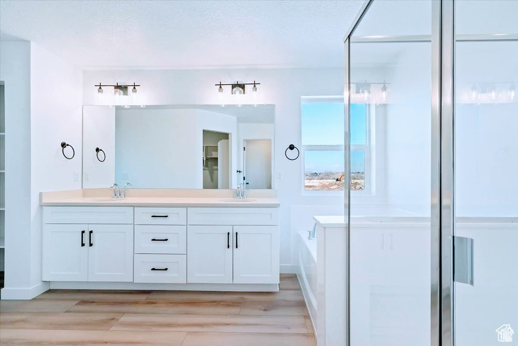 Bathroom featuring double vanity, a garden tub, a shower stall, wood finished floors, and a textured ceiling