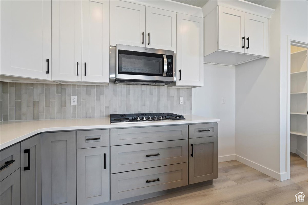 Kitchen with gray cabinets, light hardwood / wood-style flooring, stainless steel appliances, tasteful backsplash, and white cabinets