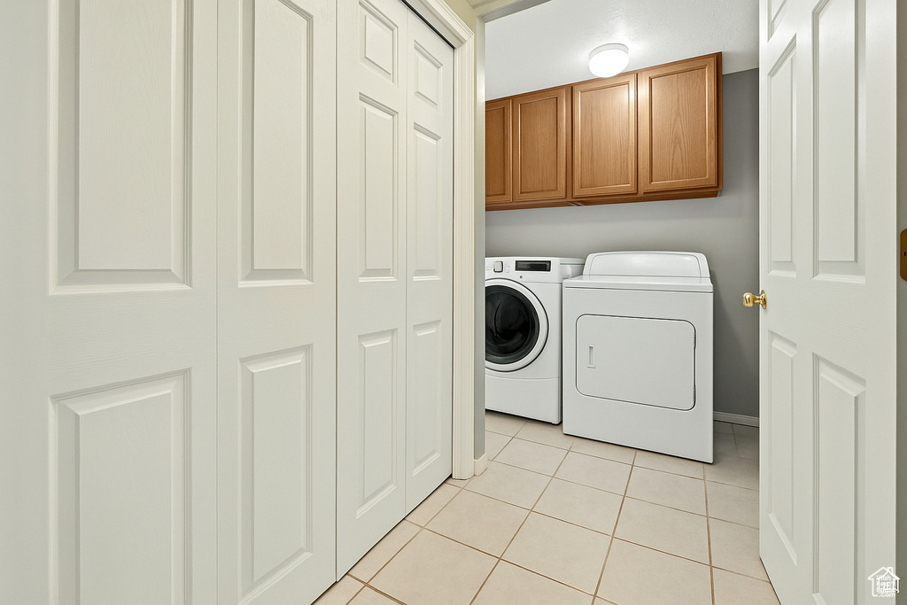 Washroom with light tile patterned floors, cabinet space, and washer and clothes dryer