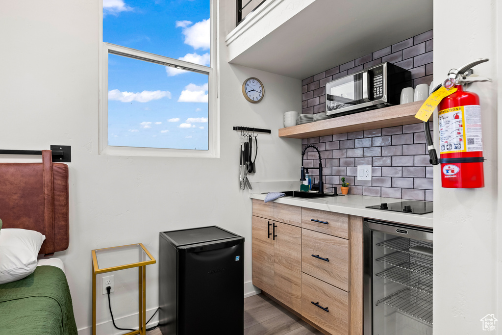 Kitchen with backsplash, fridge, beverage cooler, light hardwood / wood-style flooring, and sink