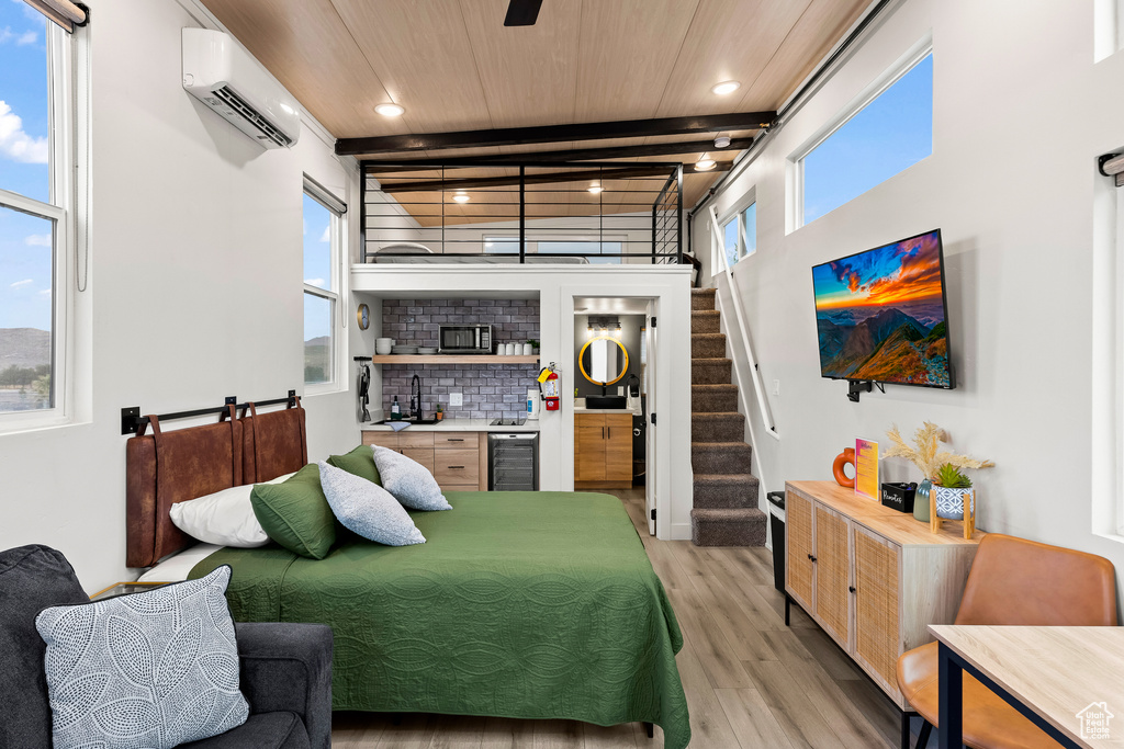 Bedroom featuring a wall mounted AC, light hardwood / wood-style floors, wine cooler, indoor bar, and beam ceiling