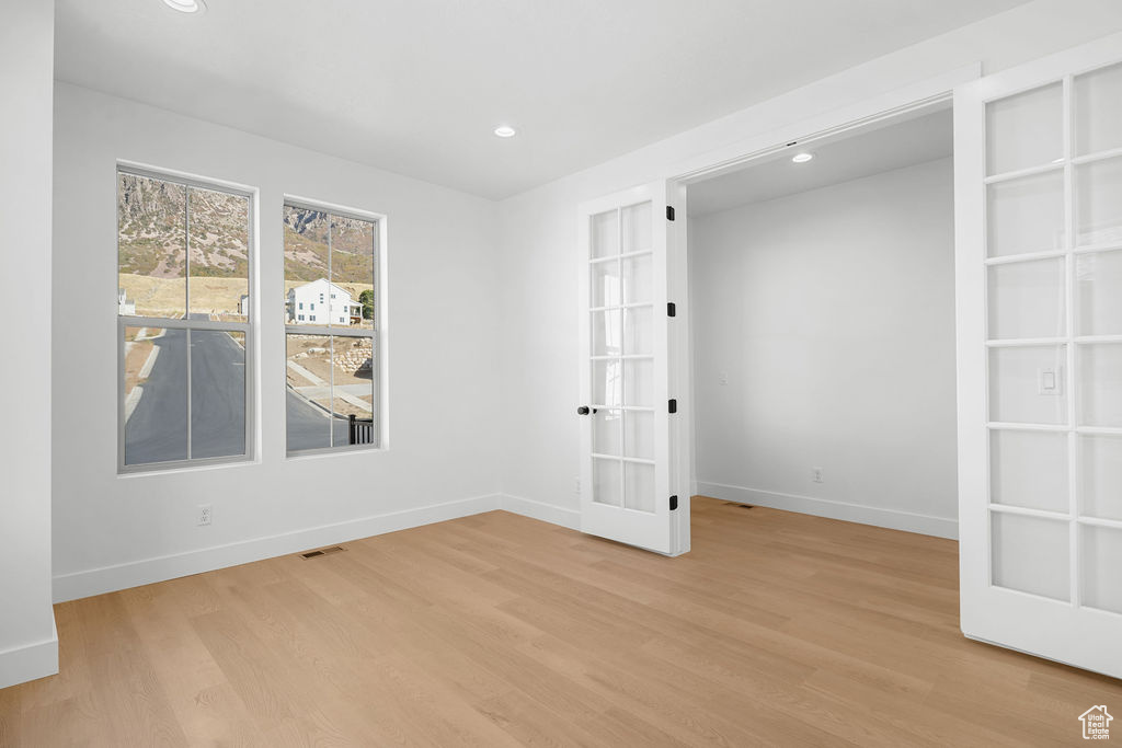 Unfurnished room with french doors, built in features, and light hardwood / wood-style floors