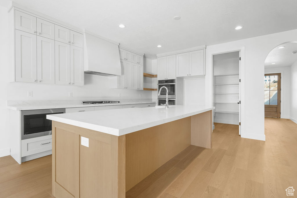 Kitchen featuring white cabinets, a kitchen island with sink, built in microwave, and light hardwood / wood-style floors