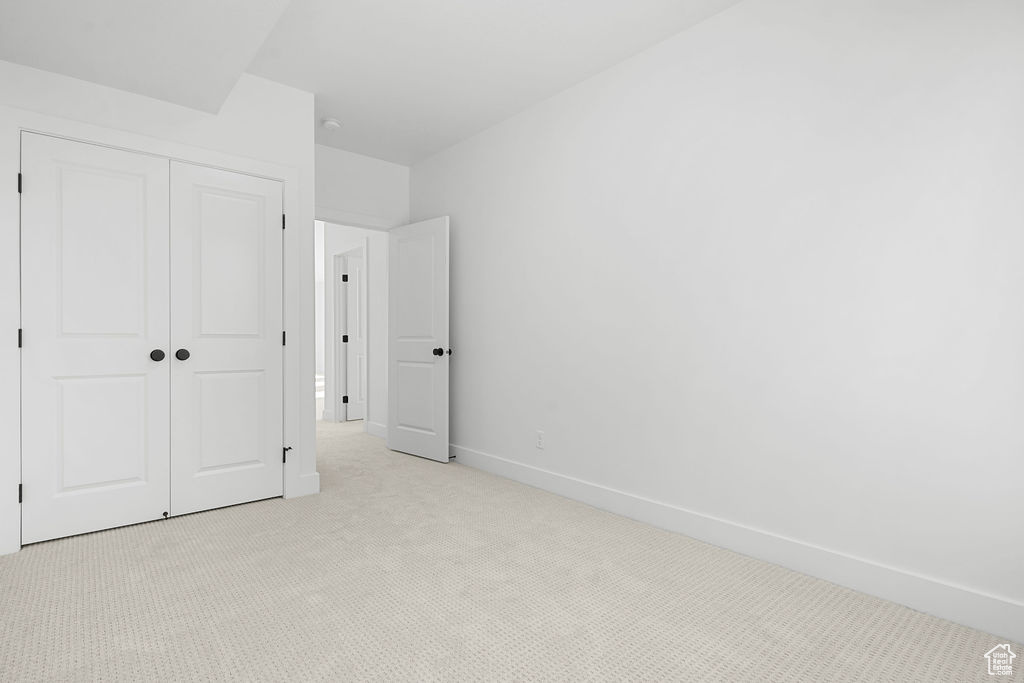 Unfurnished bedroom featuring light carpet and a closet