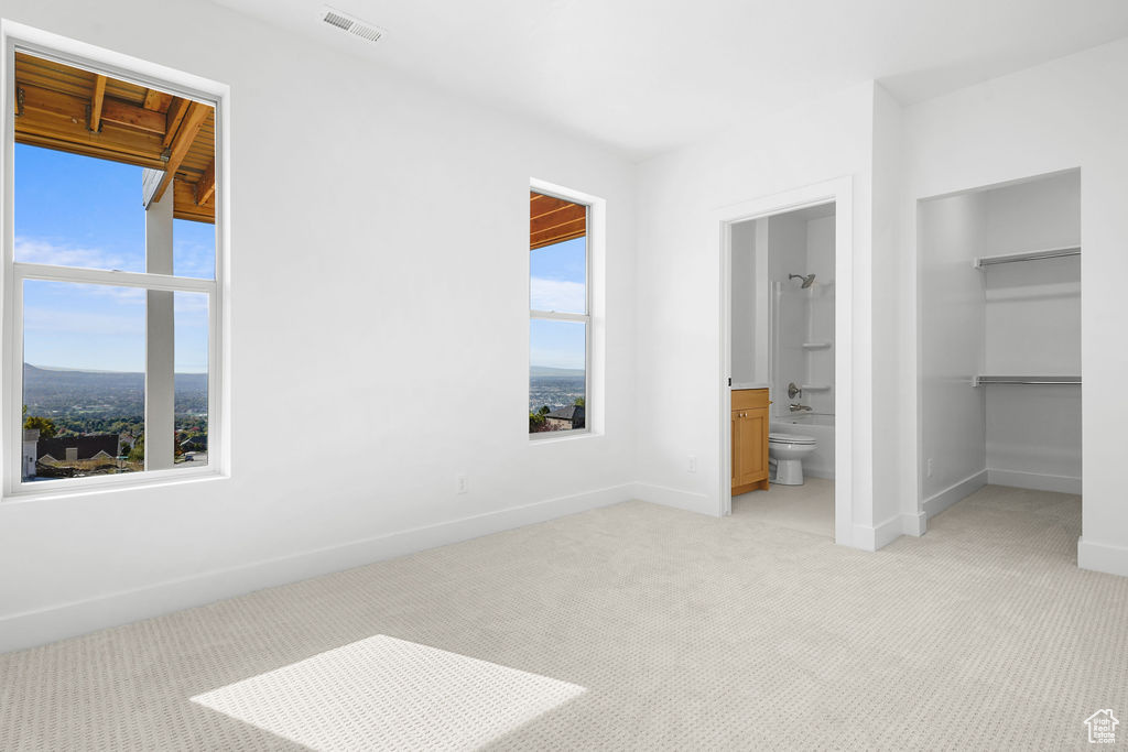 Unfurnished bedroom featuring a mountain view, light colored carpet, connected bathroom, and multiple windows