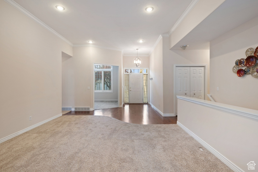 Carpeted foyer with crown molding and an inviting chandelier