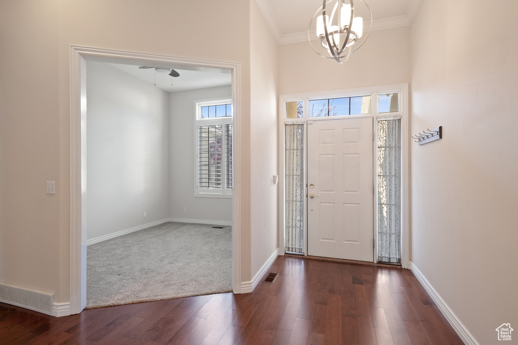 Entrance foyer featuring dark wood-type flooring, ornamental molding, and a notable chandelier