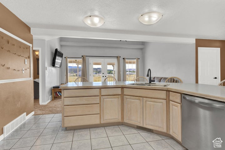Kitchen with light brown cabinetry, light tile patterned floors, stainless steel dishwasher, sink, and french doors