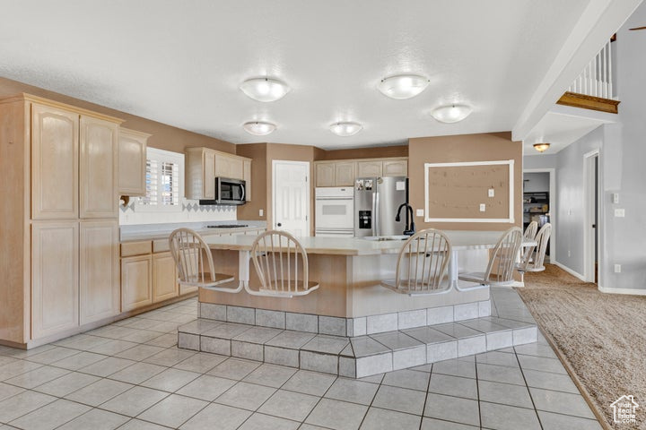 Kitchen with light brown cabinets, a center island, stainless steel appliances, and light tile patterned flooring
