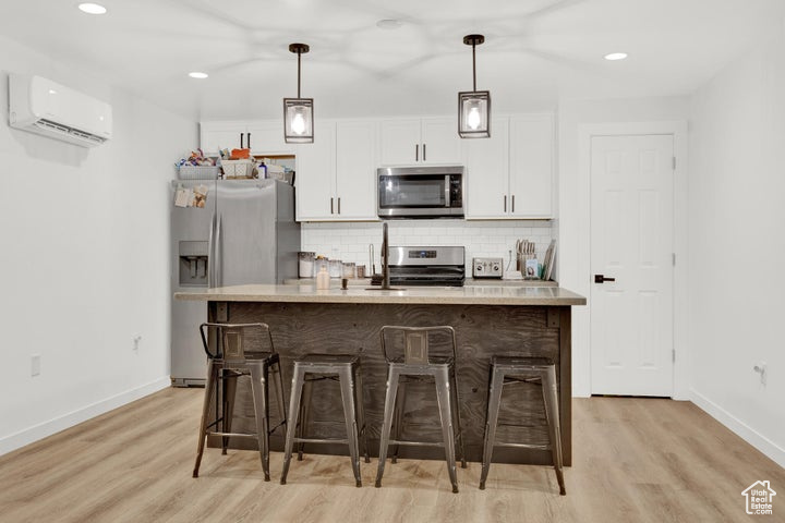 Kitchen with stainless steel appliances, white cabinetry, a center island with sink, and a wall mounted air conditioner
