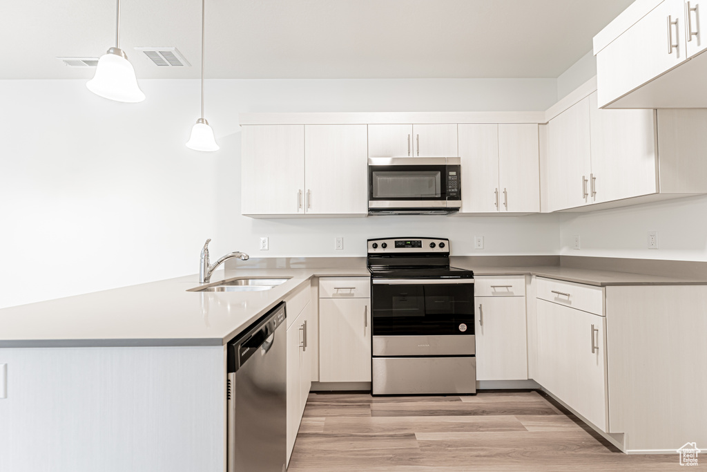 Kitchen featuring stainless steel appliances, a peninsula, light wood-type flooring, light countertops, and pendant lighting