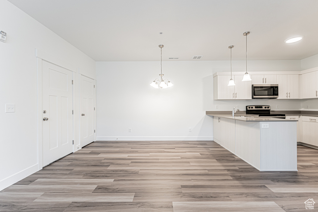 Kitchen featuring stainless steel microwave, electric range oven, light wood finished floors, and white cabinets