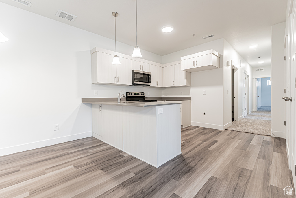 Kitchen featuring stainless steel microwave, range with electric stovetop, a peninsula, light wood finished floors, and white cabinetry