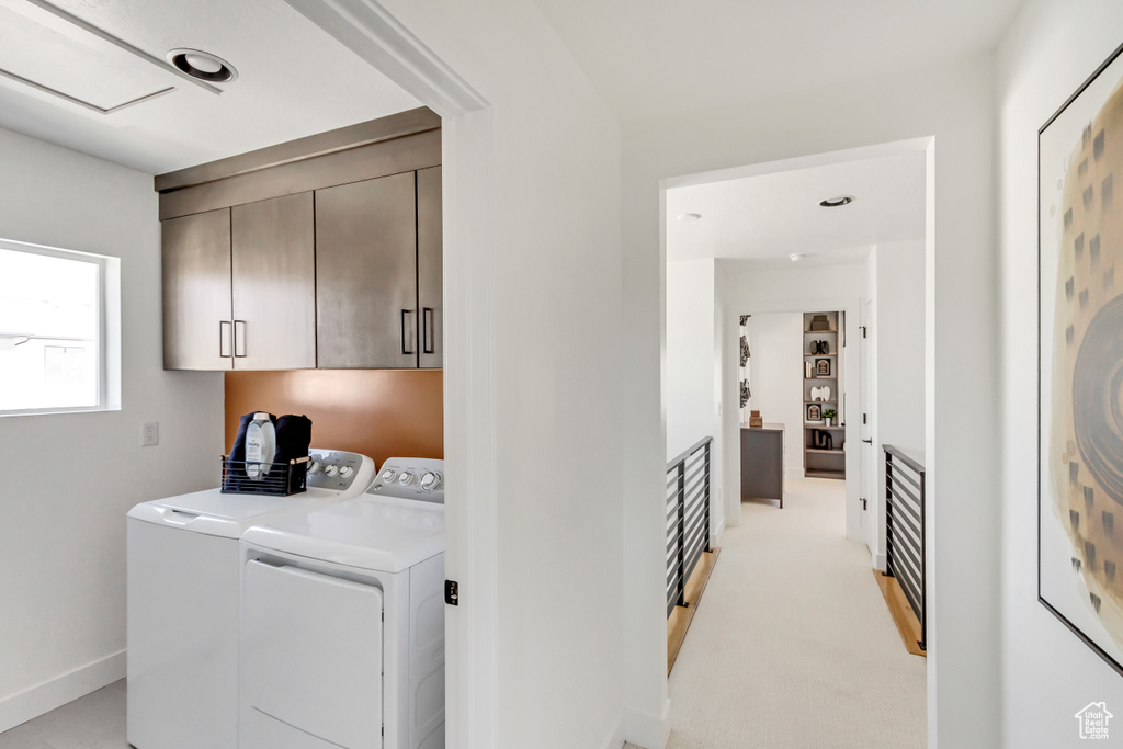 Clothes washing area featuring cabinets, light colored carpet, and washing machine and clothes dryer