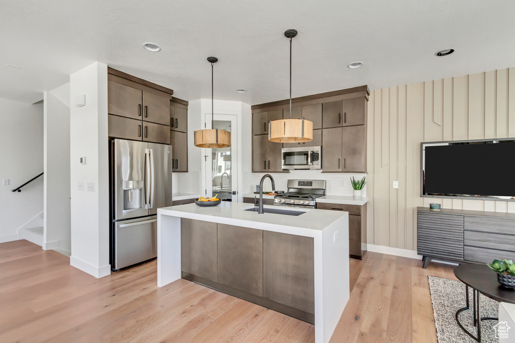 Kitchen with appliances with stainless steel finishes, an island with sink, light hardwood / wood-style floors, sink, and hanging light fixtures
