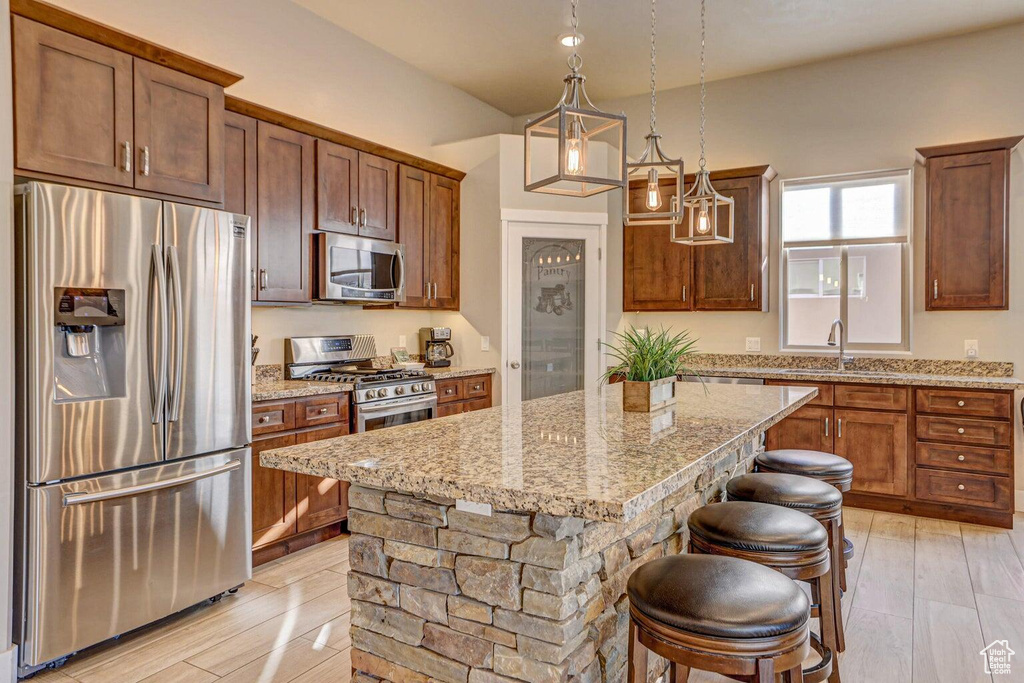 Kitchen featuring appliances with stainless steel finishes, decorative light fixtures, sink, a kitchen bar, and a kitchen island