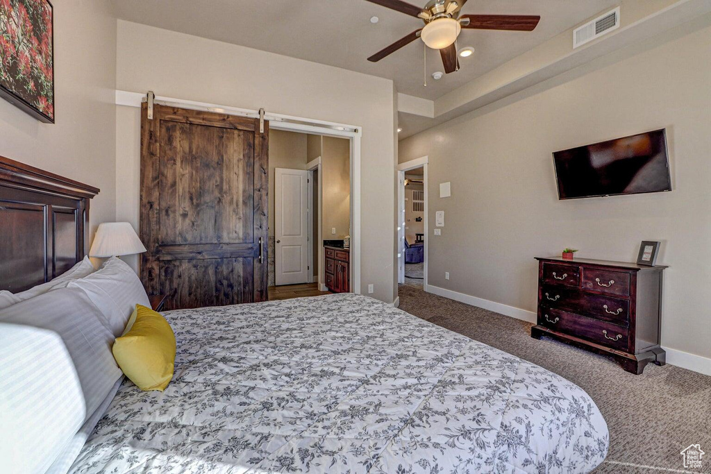 Bedroom with ceiling fan, ensuite bathroom, a barn door, and carpet floors