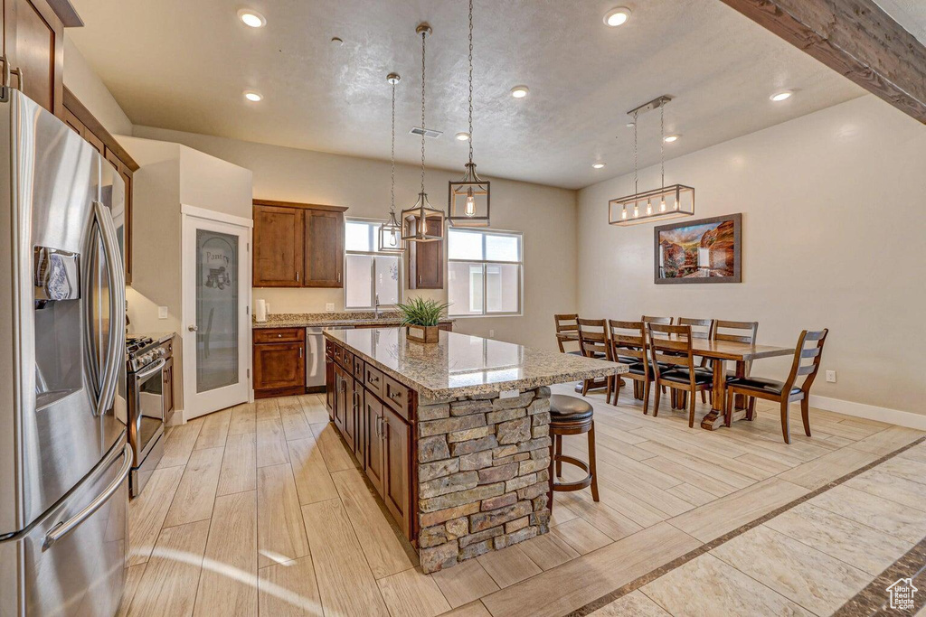 Kitchen featuring a center island, stainless steel appliances, hanging light fixtures, light stone counters, and a breakfast bar