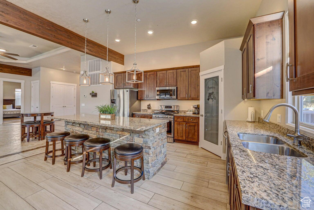 Kitchen featuring appliances with stainless steel finishes, a center island, sink, a breakfast bar, and beam ceiling