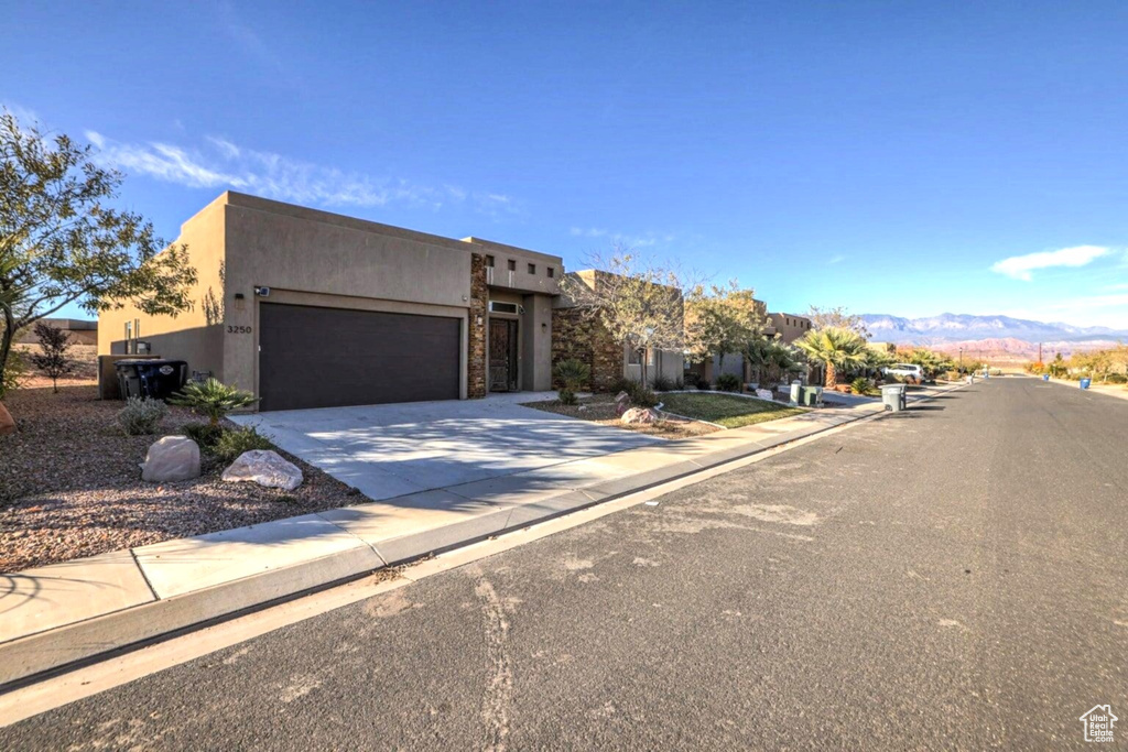 Pueblo-style house featuring concrete driveway, stucco siding, stone siding, a mountain view, and a garage
