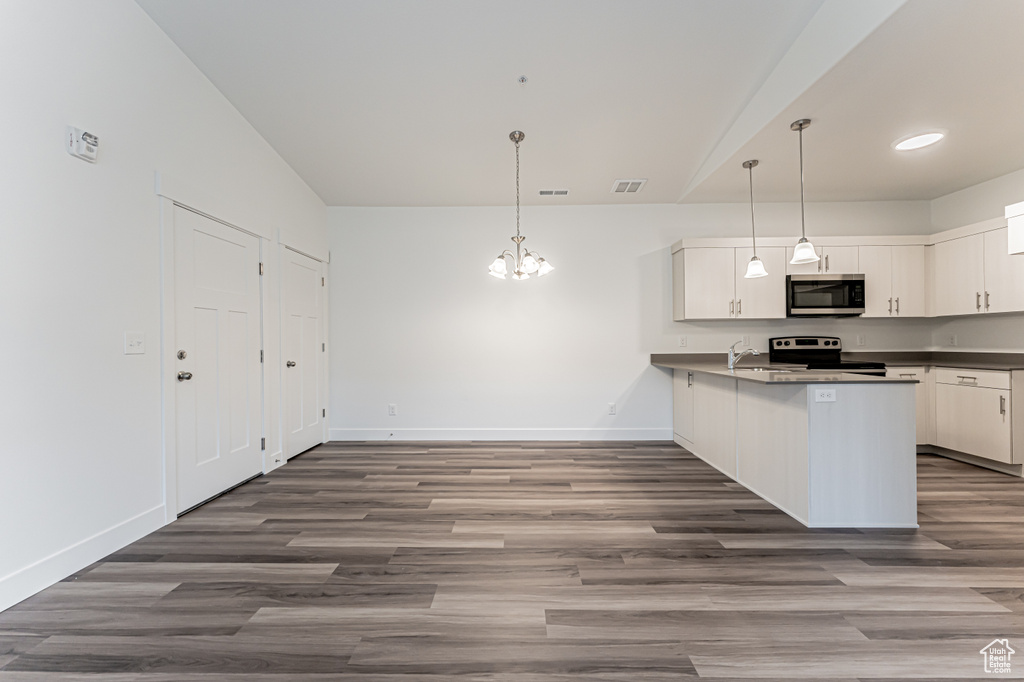 Kitchen with stainless steel appliances, a chandelier, dark countertops, a peninsula, and dark wood finished floors