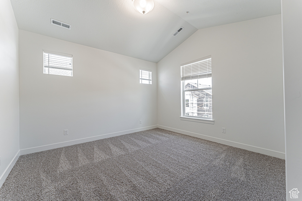 Empty room with healthy amount of natural light, lofted ceiling, and light carpet