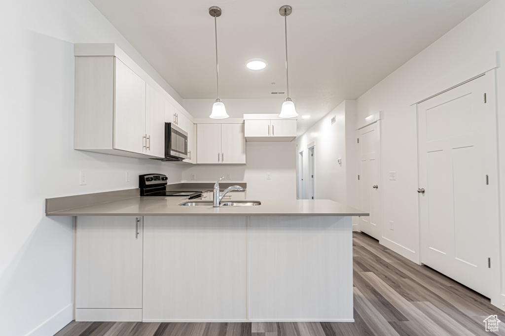 Kitchen featuring stainless steel appliances, a peninsula, wood finished floors, light countertops, and white cabinets