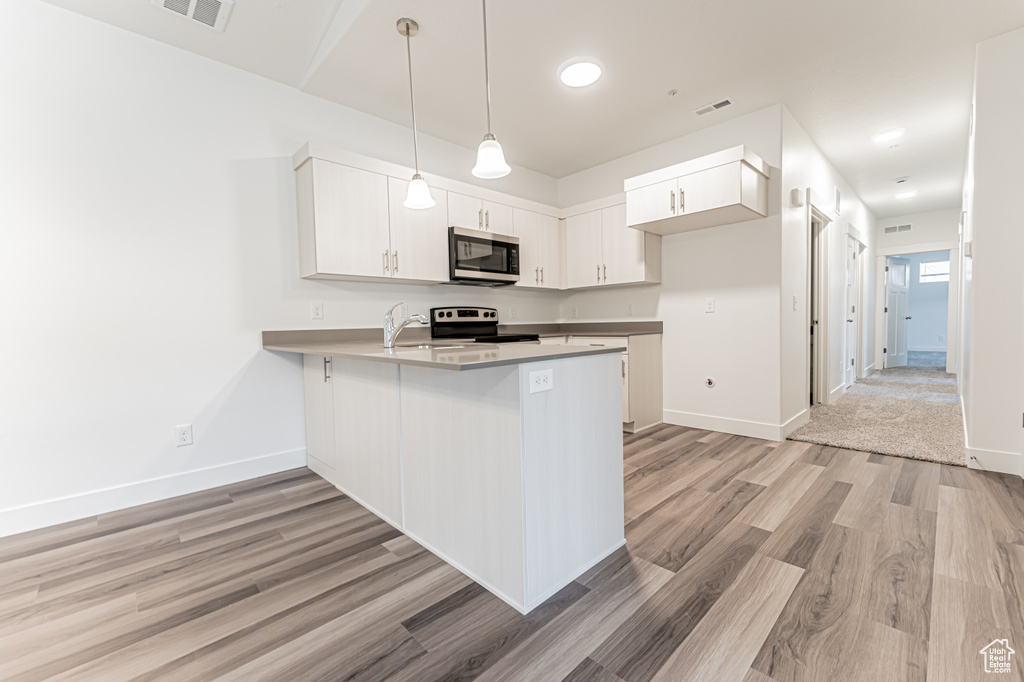 Kitchen with stainless steel microwave, a peninsula, light wood-style flooring, electric range, and white cabinets