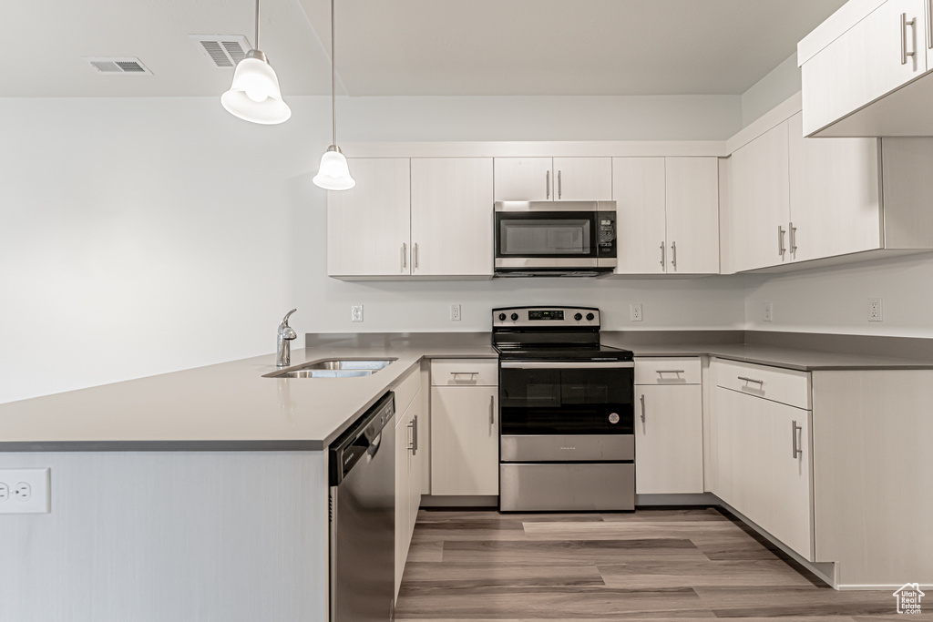 Kitchen with appliances with stainless steel finishes, a peninsula, light wood-style flooring, pendant lighting, and white cabinetry