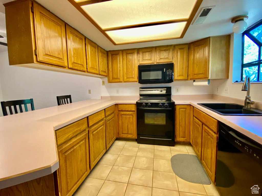 Kitchen with kitchen peninsula, light tile patterned floors, black appliances, and sink