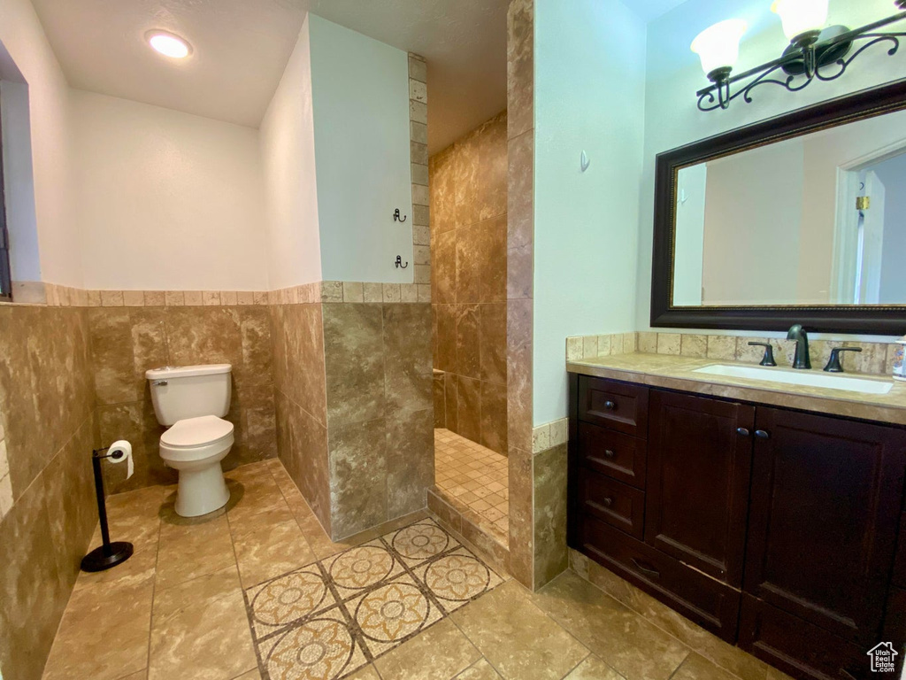 Bathroom featuring toilet, walk in shower, vanity, tile walls, and a notable chandelier