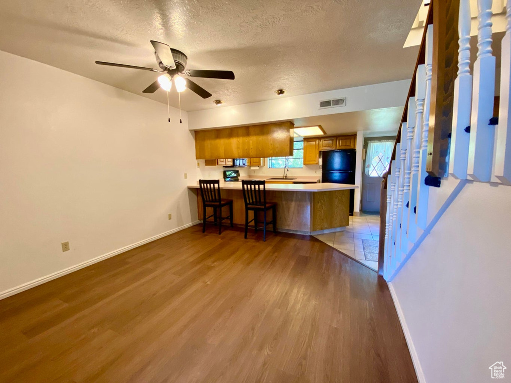 Kitchen featuring kitchen peninsula, a textured ceiling, light hardwood / wood-style flooring, black refrigerator, and a breakfast bar area