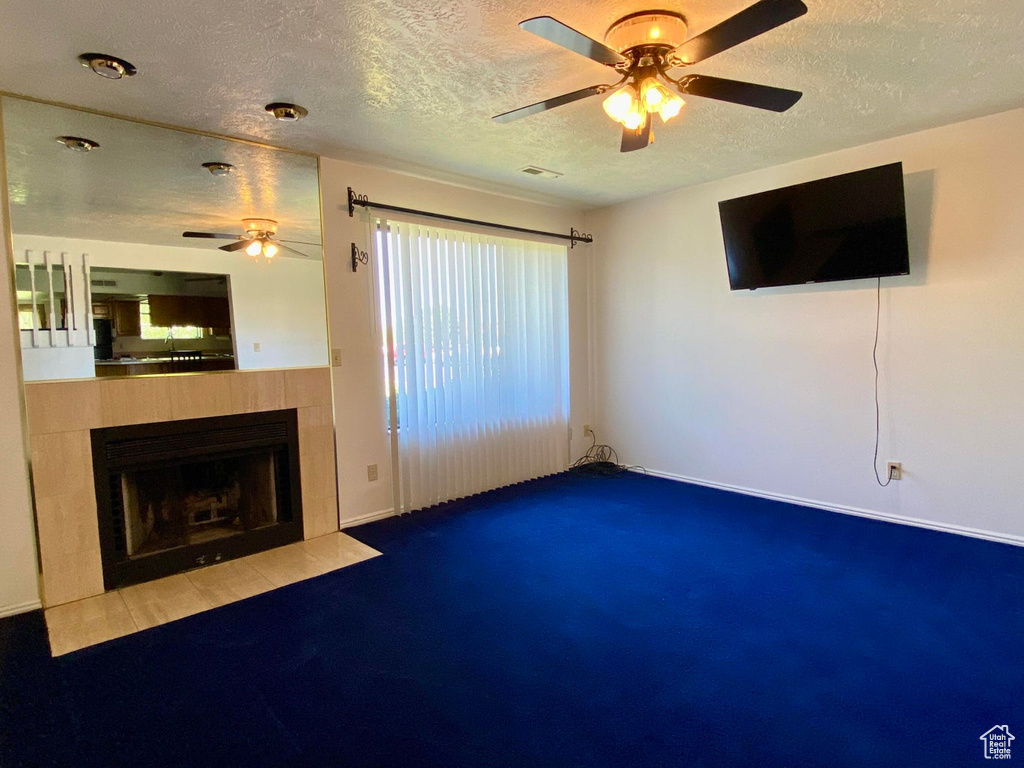 Unfurnished living room featuring carpet floors, a textured ceiling, a tiled fireplace, and ceiling fan