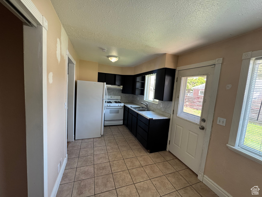 Kitchen with white appliances, a sink, a textured ceiling, dark cabinetry, and light countertops