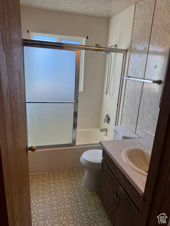 Full bathroom featuring a textured ceiling, combined bath / shower with glass door, vanity, and toilet