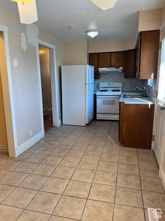 Kitchen featuring white appliances, dark brown cabinetry, a textured ceiling, sink, and light tile patterned floors