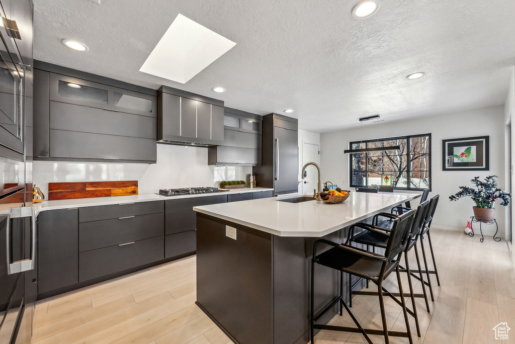 Kitchen featuring a kitchen breakfast bar, sink, a kitchen island with sink, a textured ceiling, and a skylight