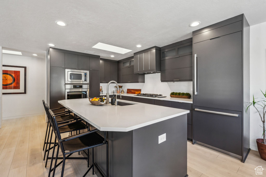 Kitchen with sink, a breakfast bar, a center island with sink, light hardwood / wood-style floors, and built in appliances