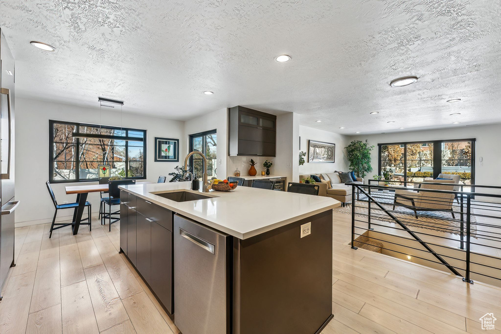 Kitchen featuring plenty of natural light, a textured ceiling, dishwasher, and an island with sink