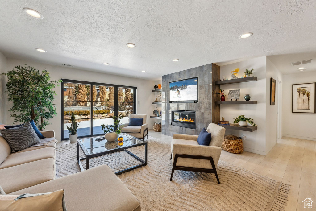 Living room with light hardwood / wood-style floors, a textured ceiling, and a tiled fireplace