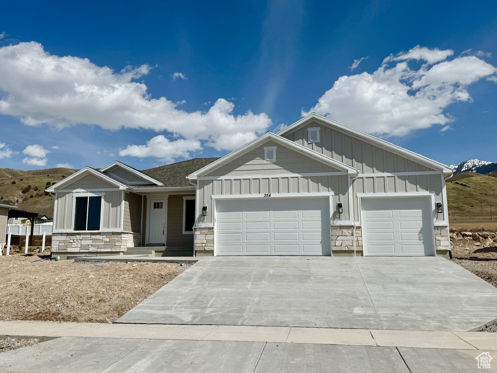 View of front facade with stone siding, board and batten siding, concrete driveway, and a garage