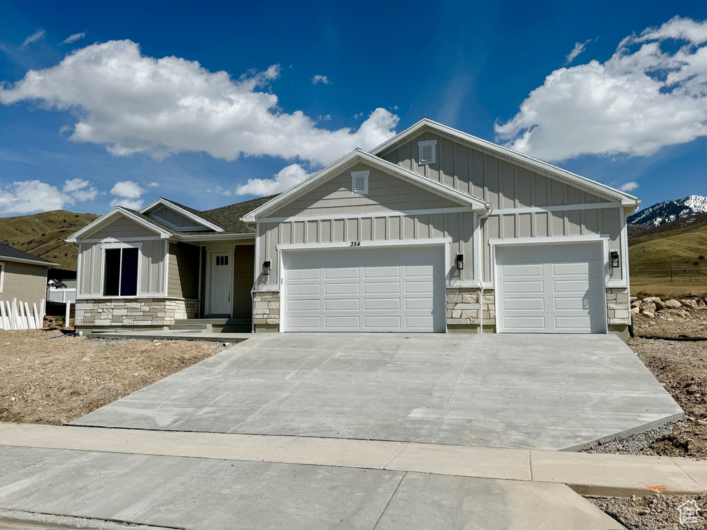 Craftsman-style home featuring driveway, stone siding, an attached garage, and board and batten siding