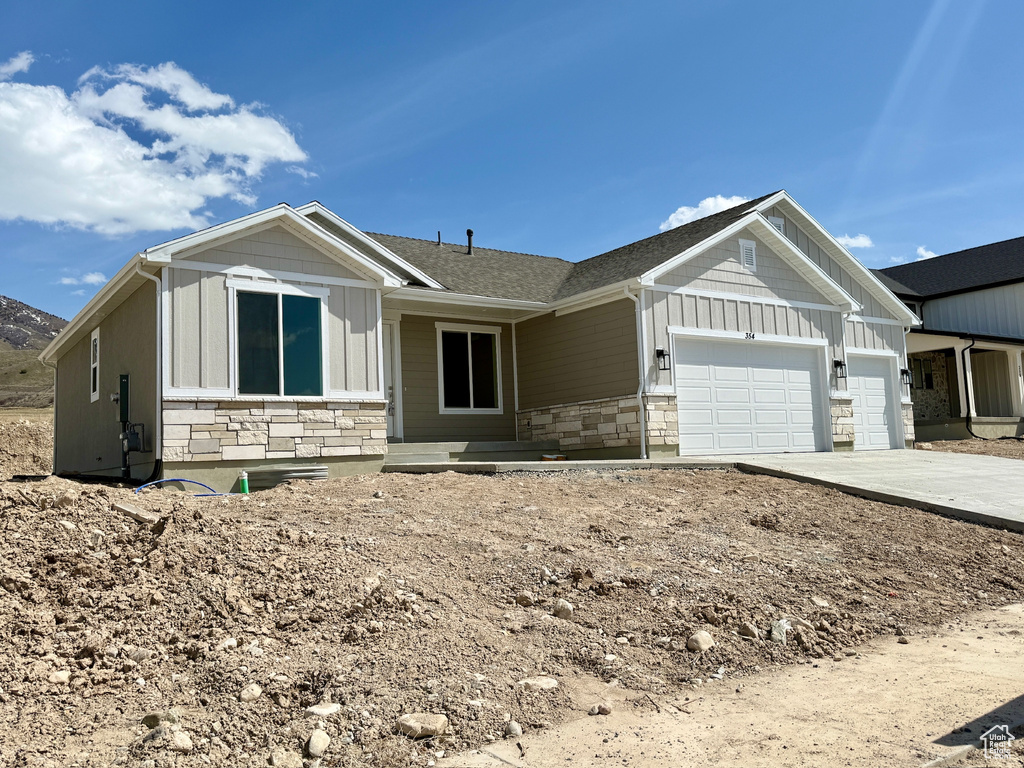 View of front of home with concrete driveway, board and batten siding, an attached garage, and stone siding
