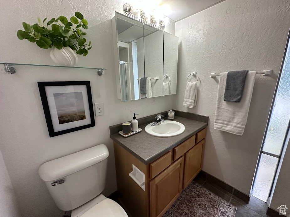 Bathroom with vanity, toilet, tile patterned floors, and a textured wall